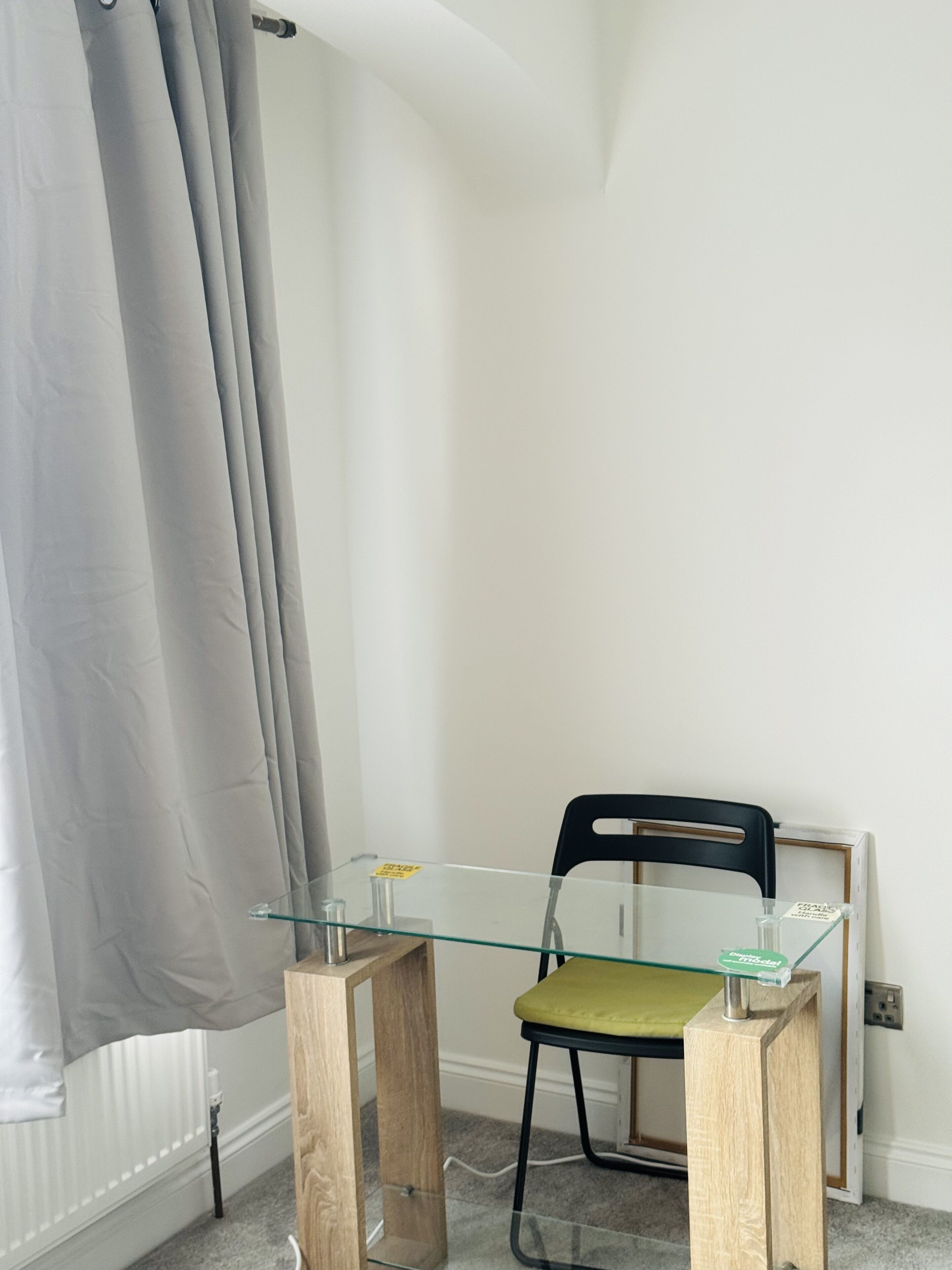 A small, modern room with a glass-top table, a wooden chair, and a radiator.