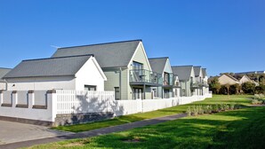 A row of modern, single-story houses with a white picket fence, a paved driveway, and a well-maintained lawn. - 3 bedroom accommodation in Westward Ho! (Westward Ho!)