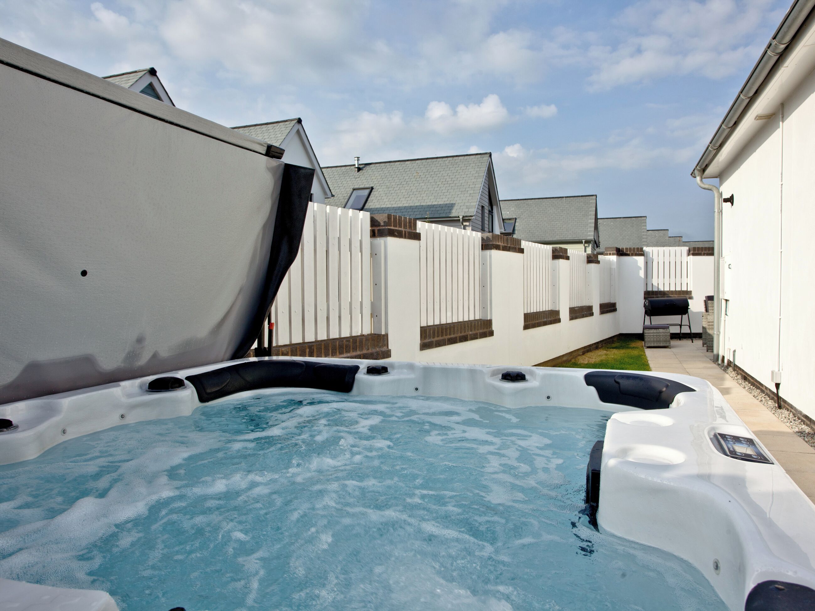 A backyard with a hot tub, a white fence, and a barbecue grill.