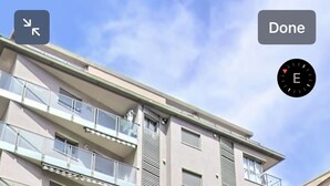 Ein mehrstöckiges Gebäude mit Balkonen und einem Ladenlokal im Erdgeschoss mit Glasauslagen.