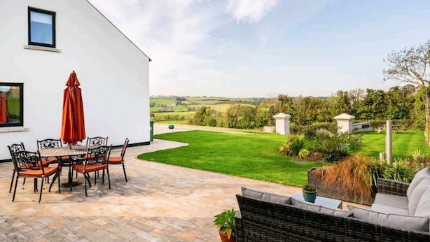 Un patio con una mesa y sillas, un sofá de mimbre y vistas a un paisaje verde.