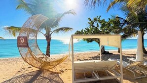 Eine Strandlandschaft mit einer Hängematte, Liegestühlen und einer Sonnensegel-Konstruktion.