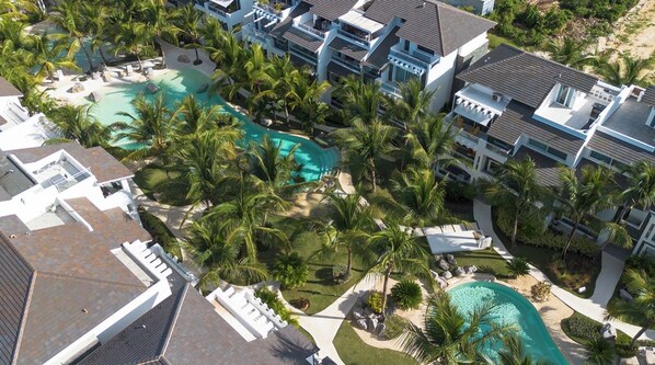 A resort with multiple buildings, a central swimming pool, and surrounding palm trees.