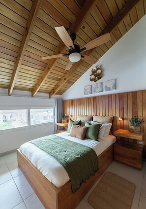 A bedroom with a wooden ceiling, a bed with multiple pillows, a nightstand, and a ceiling fan.