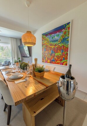 Ein Essbereich mit einem Holztisch, gedeckt für vier Personen, einer modernen Pendelleuchte und einem großen, farbenfrohen Gemälde an der Wand.