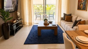 Ein modernes Wohnzimmer mit Fernseher, Sofa, Esstisch und einem Balkon mit Vorhängen.