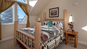A bedroom with a wooden bed, a quilt, a nightstand, a lamp, and a painting on the wall. - Backwater Retreat Townhome Walk to Ski Shuttle (Driggs)