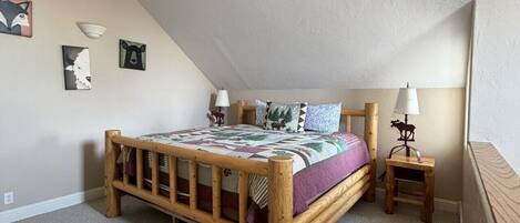 Un dormitorio con cama de madera, una mesita de noche, lámpara y decoración en la pared.