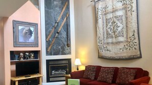 A living room with a red sofa, a television on a wooden stand, a fireplace, and a large tapestry. - Backwater Retreat Townhome Walk to Ski Shuttle (Driggs)