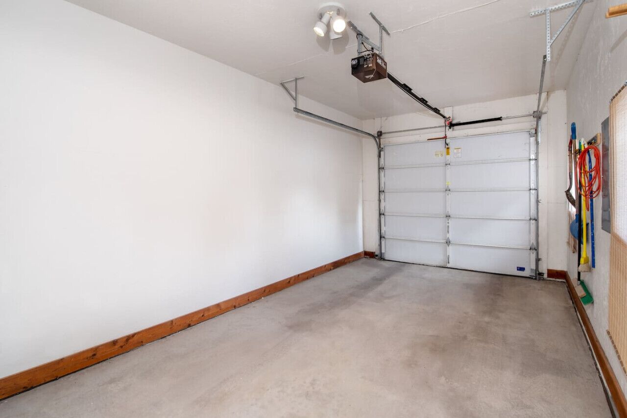 A clean, empty garage with a white door, a ceiling-mounted light fixture, and some tools hanging on the wall.