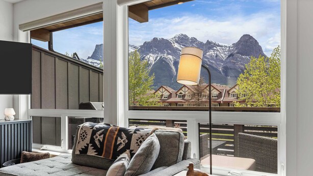 Una sala de estar acogedora con un sofá, una lámpara y vistas a montañas a través de grandes ventanales.