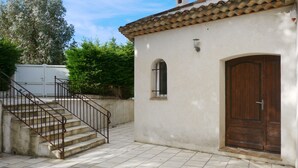 A building with a tiled roof, a wooden door, and a small window. There is a staircase with a metal railing leading to a concrete wall. - Country villa - Sleeps 8 - Mimosa view (Tanneron)