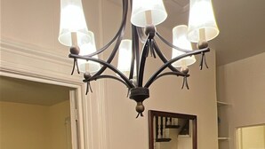 A foyer with a black and white checkered floor, a wooden staircase, and a chandelier with multiple lamps. - Charming Brick Home in Seneca Falls Historic District! (Seneca Falls)