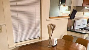 A dining table with six chairs, a vase with flowers, and a kitchen area in the background. - Charming Brick Home in Seneca Falls Historic District! (Seneca Falls)