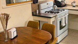 A modern kitchen with a stove, oven, and white cabinets. There is a dining table with chairs and a vase of dried flowers. - Charming Brick Home in Seneca Falls Historic District! (Seneca Falls)
