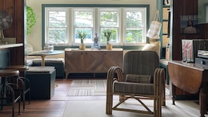 Een gezellige woonkamer met een houten bank, een gestreept fauteuil en een groot raam met veel ruitjes.
