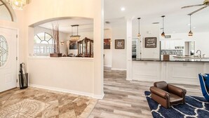 A spacious living area with a modern kitchen, a chandelier, and a blue armchair. - Shore Drive Sunshine fully furnished home pet friendly (Oldsmar)