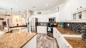 A modern kitchen with white cabinets, granite countertops, stainless steel appliances, and a black and white backsplash. - Shore Drive Sunshine fully furnished home pet friendly (Oldsmar)