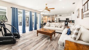A spacious living room with a treadmill, a white sofa, and a wooden coffee table. - Shore Drive Sunshine fully furnished home pet friendly (Oldsmar)