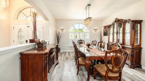 A dining room with a long wooden table, chairs, a chandelier, and a large wooden cabinet. - Shore Drive Sunshine fully furnished home pet friendly (Oldsmar)