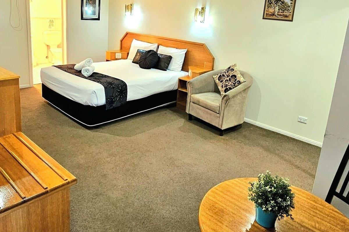 A hotel room with a bed, a chair, a small table with a plant, and a wooden desk.