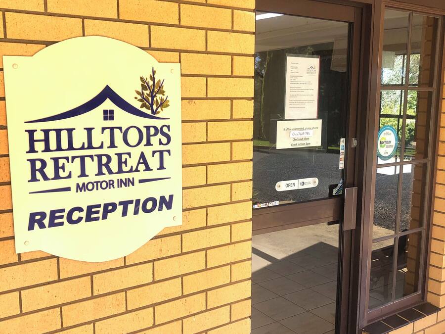 A brick building with a sign for Hilltops Retreat Motor Inn Reception.