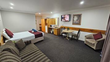 Habitación de hotel con dos camas, un sofá, una mesa de comedor con sillas, un microondas y una pequeña kitchenette.