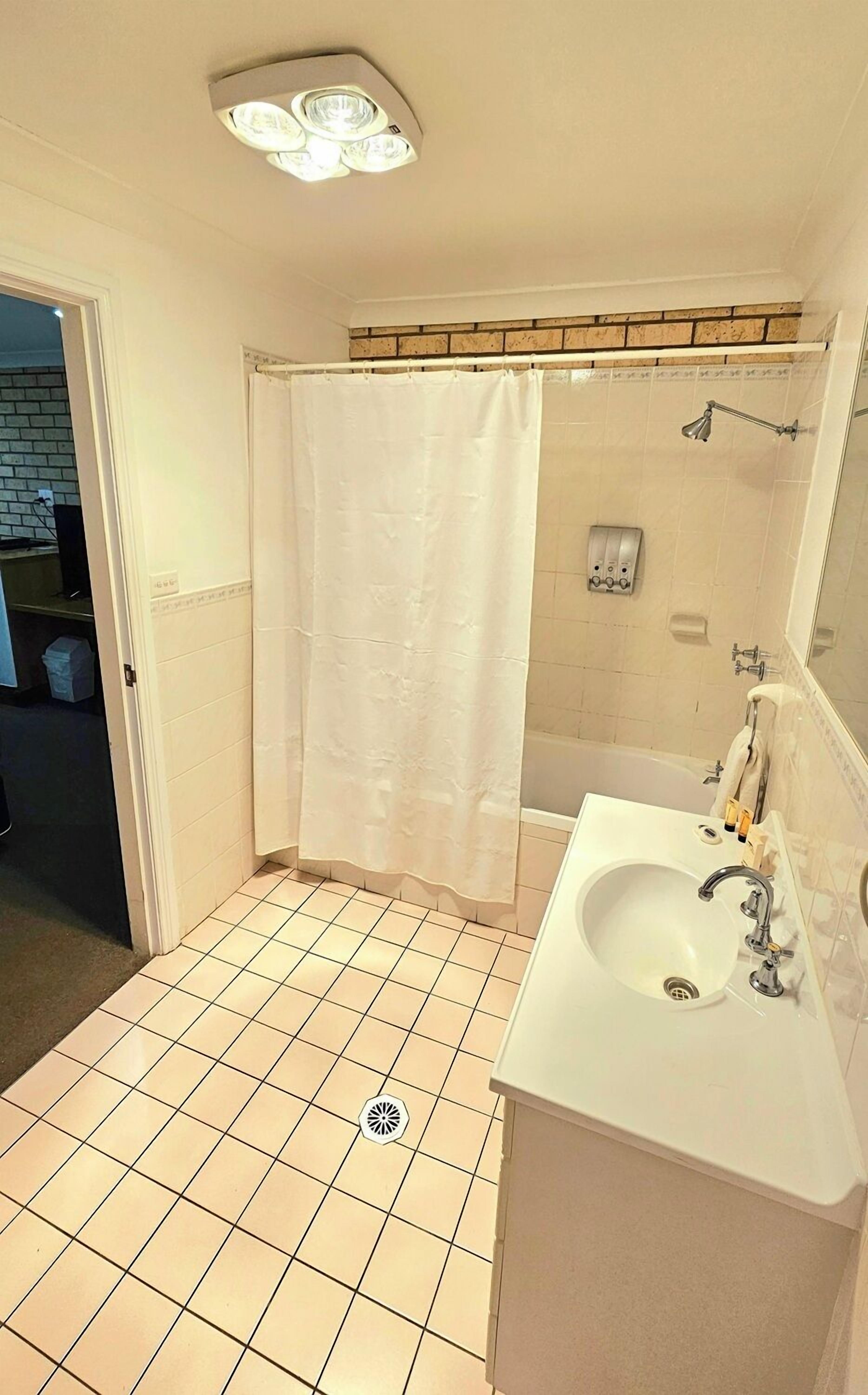 Een badkamer met een wit wastafelmeubel, douchegordijn en een bad.