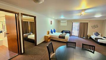 A hotel room with a bed, a sofa, a dining table, and a chair.