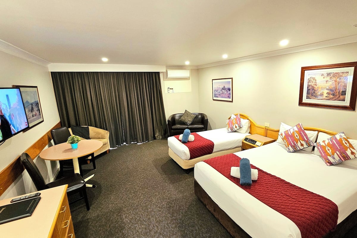 A hotel room with two beds, a desk, a chair, a TV, and a window with curtains.