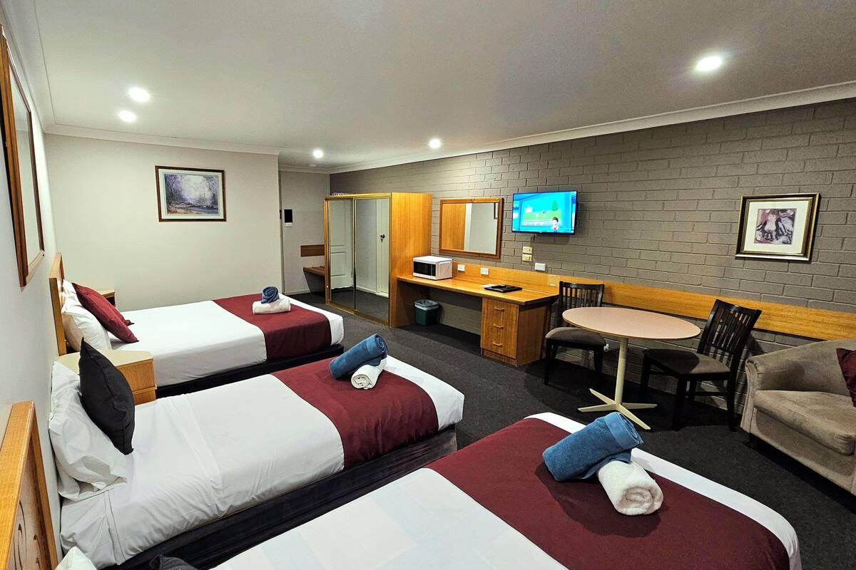 A hotel room with two single beds, a desk with a chair, a small table, a TV, and a brick wall.