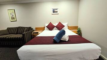 A hotel room with a bed, a sofa, a nightstand, and a small table.