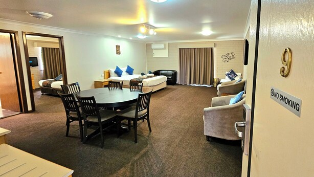 A hotel room with a dining area, a sofa, and a chair. There is a sign on the wall indicating no smoking. - Hilltops Retreat Motor Inn (Young)