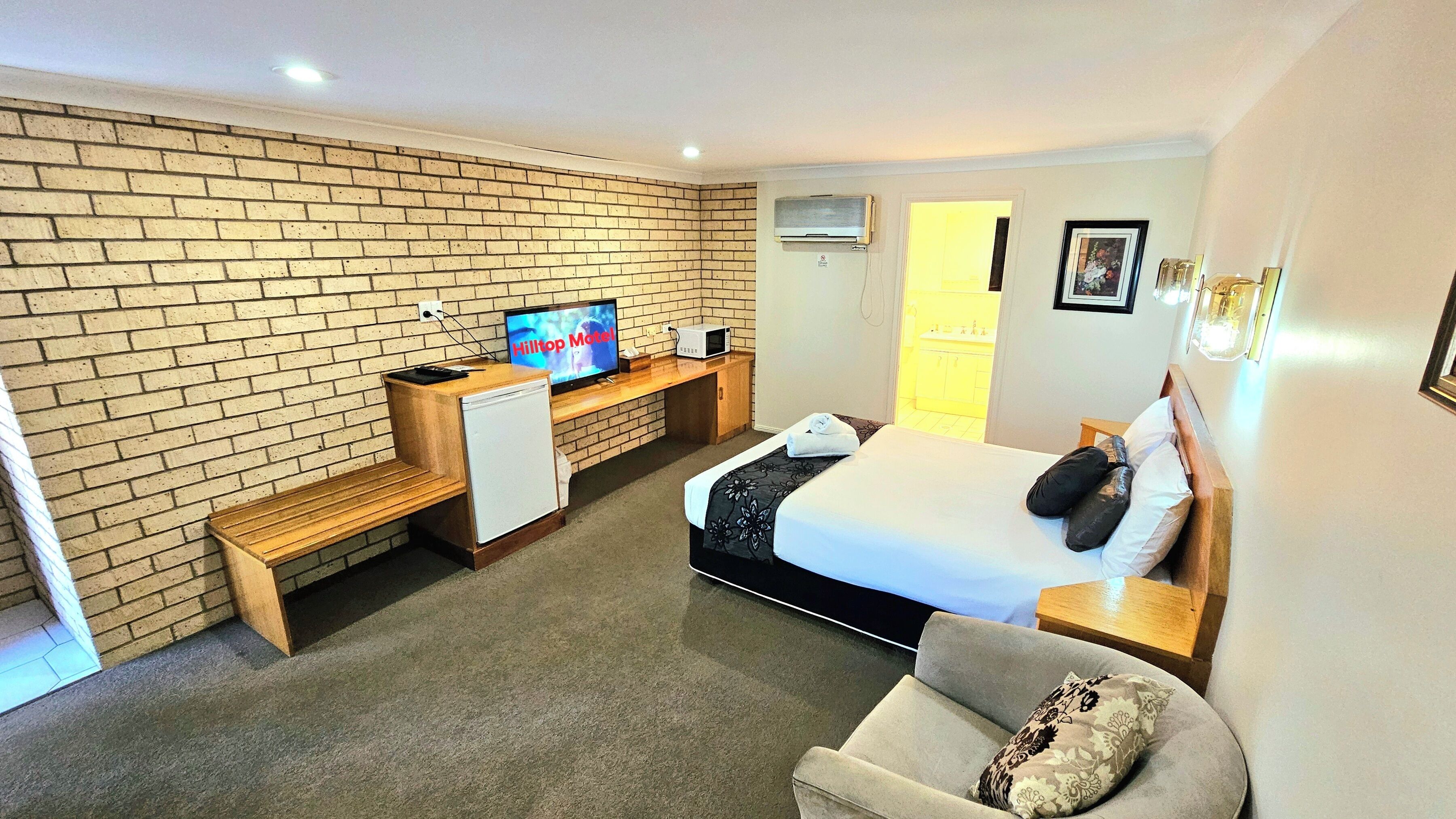 Hotelkamer met een bakstenen muur, een bed, een bureau met een televisie, een magnetron en een kleine koelkast.