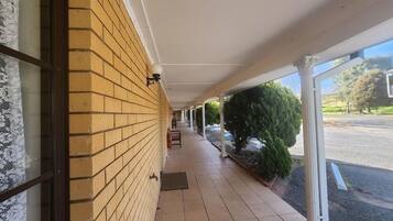 A covered walkway with a brick wall and a tiled floor, leading to a building entrance.