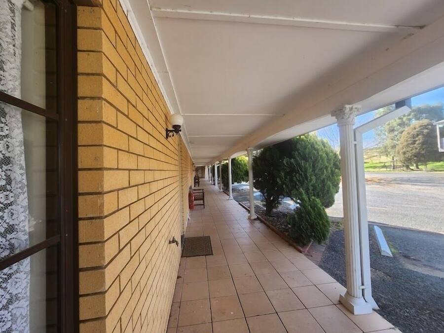 A covered walkway with a brick wall and a tiled floor, leading to a building entrance.