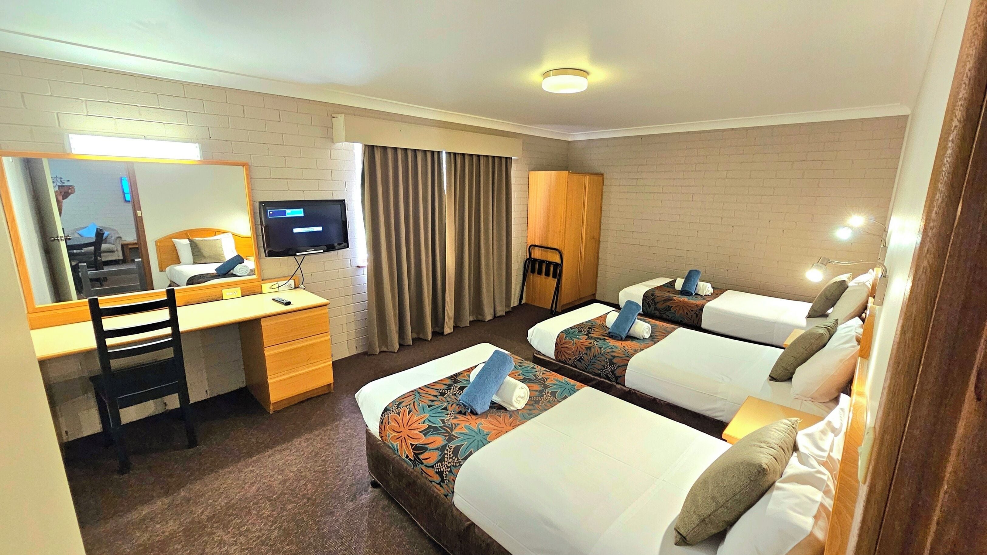 Habitación de hotel con dos camas, un escritorio, una silla, un televisor y un espejo.
