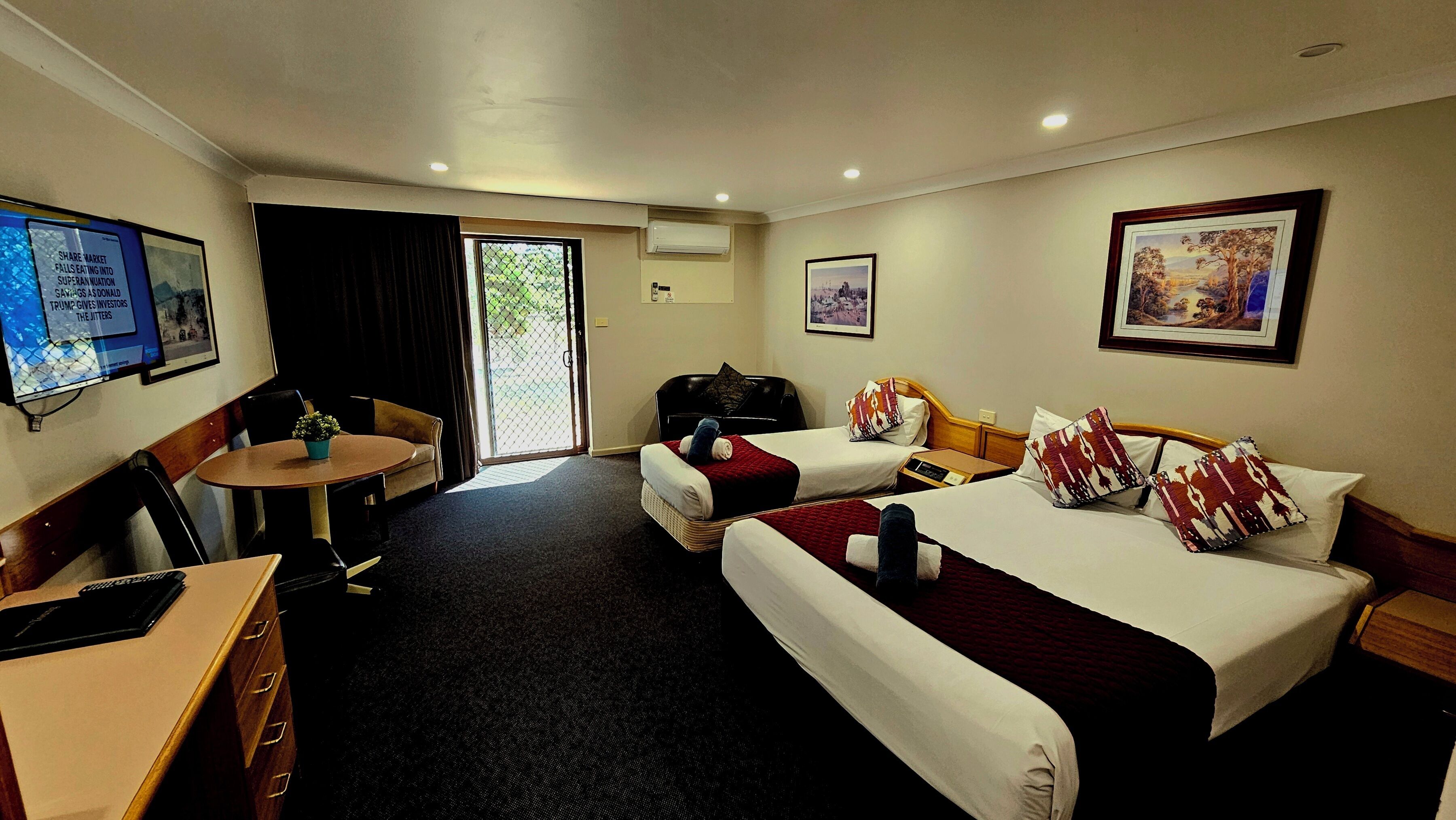 A hotel room with two beds, a desk, a chair, a small table, and a TV.