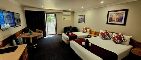 A hotel room with two beds, a desk, a chair, a small table, and a TV.