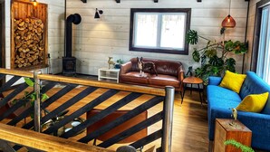 Un salon chaleureux avec un canapé en cuir marron, un canapé bleu agrémenté de coussins jaunes, un escalier en bois et une grande fenêtre.
