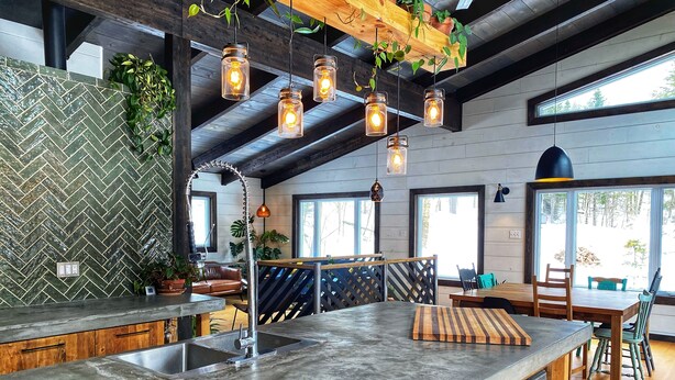 Une cuisine moderne dotée d’un grand îlot central, de tabourets de bar en bois et de luminaires suspendus.
