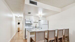 A modern kitchen with white cabinets, a microwave, a stove, and a refrigerator. There are four wooden bar stools at the kitchen island. - 2024 updated condo with water views! (Treasure Island)