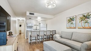 A modern living room with a grey sofa, a TV, and artwork on the wall. - 2024 updated condo with water views! (Treasure Island)