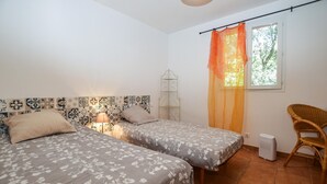 Quarto com duas camas, uma janela com cortinas laranja, uma cadeira de vime e um radiador.