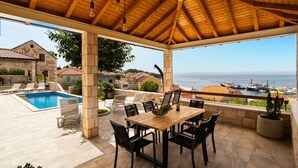 A covered outdoor area with a pool, dining table, and chairs, overlooking a harbor with boats. - Beautiful home in Sumartin with sauna (Sumartin)