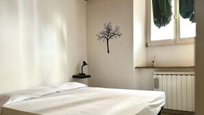 A bedroom with a bed, a wall-mounted lamp, a radiator, and a window with curtains. - SE080 - Senigallia, comfortable four-room apartment in the historic center (Senigallia)