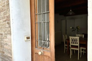 Eine Holztür mit Fenster, ein Essbereich mit weißen Stühlen und einem Tisch sowie eine hängende Leuchte.