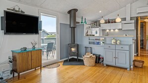 A modern kitchen with a wood-burning stove, a dining area with chairs, and a TV mounted on the wall. - Nice home in Lemvig with WiFi (Lemvig)