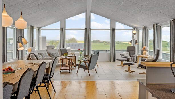 A spacious room with a high ceiling, large windows offering a view of the countryside, a dining area with a wooden table and chairs, and a seating area with sofas and armchairs. - Nice home in Lemvig with WiFi (Lemvig)