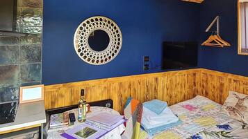 A room with a wooden headboard, a circular wall decoration, a bed with floral bedding, a table with a laptop, and a hanging clothes rack.